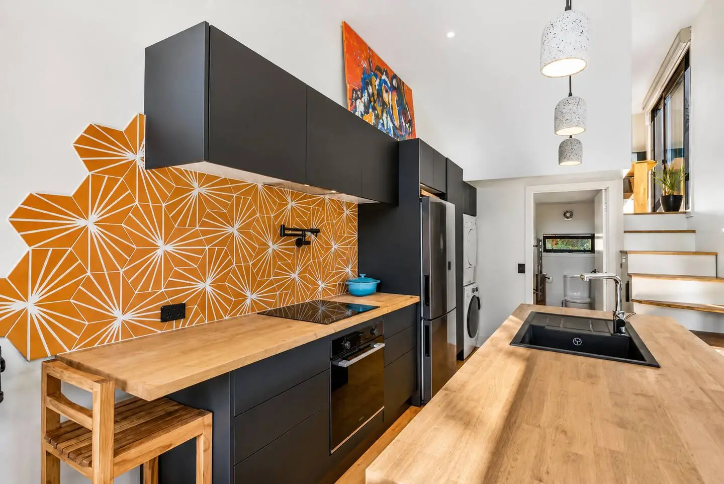 Kitchen with black cabinetry, wood countertops, and a bold orange geometric tile backsplash.
