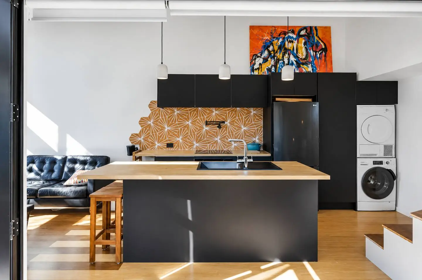 Kitchen island with wood countertop and pendant lighting, opening to the living area and stacked laundry.